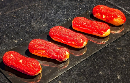 Striking red-glazed eclairs presented on a sleek black serving tray over a dark reflective surface.