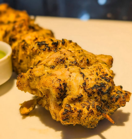 Grilled tandoori chicken skewers marinated in spices and served with vibrant mint chutney, sautÃ©ed onions and bell peppers on a white square plate.の写真素材