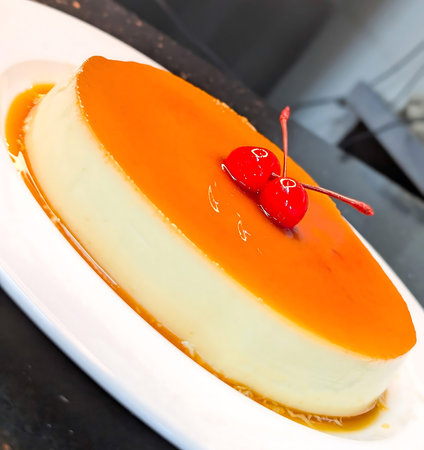 Classic flan custard topped with glossy caramel and two maraschino cherries, presented on a white...