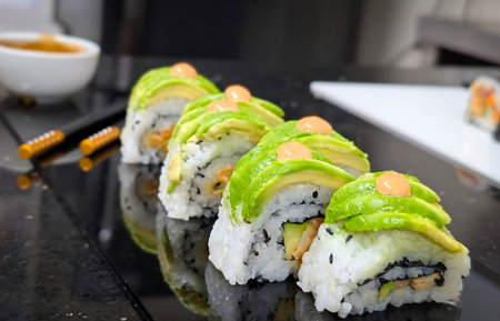 Avocado topped sushi roll with seasoned rice, sesame and nori, finished with a small orange sauce dollop and cooked seafood filling.の写真素材