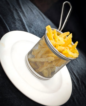 Crispy French fries seasoned with herbs and chili flakes served in a metal mesh basket on a white...