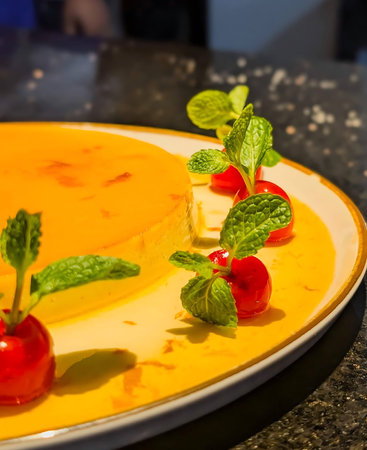 Classic flan with caramelized sugar and bright cherries, finished with fresh mint on a white gold...