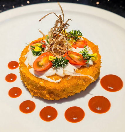 Golden breaded croquette topped with creamy sauce, halved cherry tomatoes, parsley and crispy fried...
