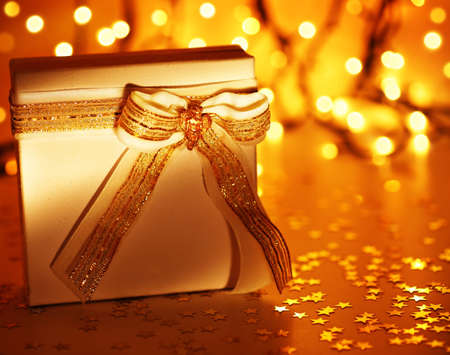 Gold holiday background with white present gift box, Christmas ornament and new year decoration over defocused lightsの写真素材