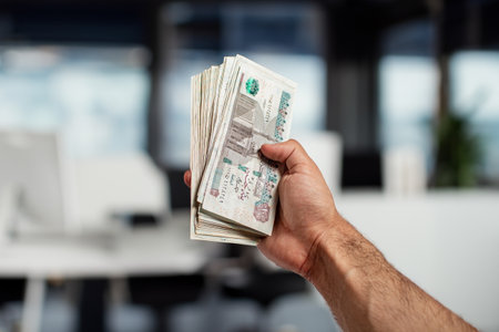 Man arm Holding bundles of Egyptian money currency 100 pound on office Backgroundの写真素材