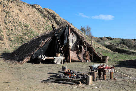 A reed tent on a mountain slope. There are old furniture and fire in front of the tent.の写真素材