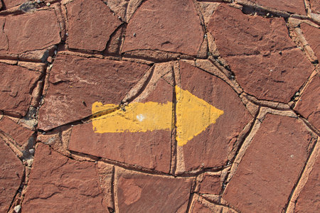 A wall made of brown shapeless stones. There is a yellow sign arrow on the wall indicating the right...