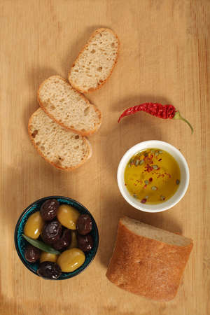 Green and black olives in porcelain bowl with olive oil  with fresh bread, young olive branch ,...