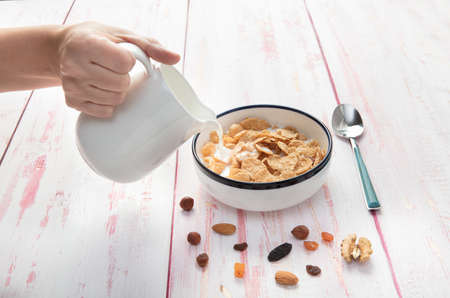 Pouring milk on a bowl of cornflakes  , hazelnut, dry apricot, walnut and nuts on wooden background , top view,  close-upの写真素材