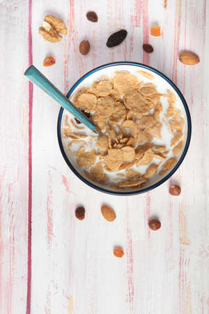 Bowl of cornflakes and milk, hazelnut, dry apricot, walnut and nuts on wooden background , top view,...