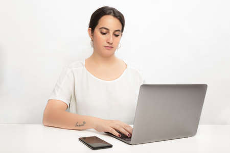 Studio shot portrait of a woman working with concentration on a wireless laptop next to her mobile...