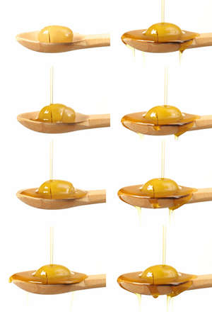 Olive oil pouring off a wooden spoon with a green olive on it in a series of eight different views isolated on whiteの写真素材