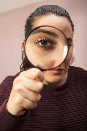 Woman searching for clues or conducting an investigation or search peering through a handheld magnifying glass , what makes his eye seem biggerの写真素材
