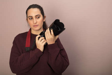 Woman photographer holding a camera and lens looking thoughtfully to the side towards blank copy spaceの写真素材