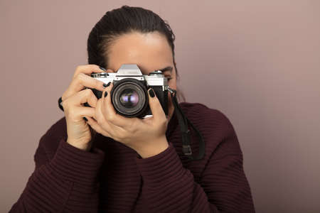 Young woman focusing on the viewer and taking picture with a vintage cameraの写真素材