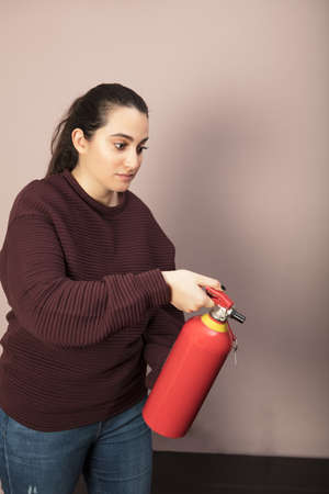 Determined woman holding a red fire extinguisher pointed ahead of her towards the floor indoors in a buildingの写真素材
