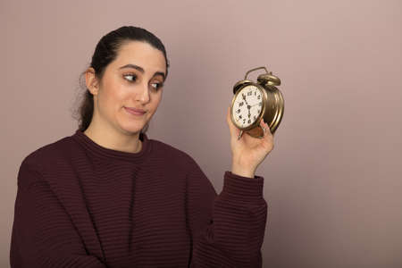 Young woman looking dubiously at an alarm clock with a look of contemplation as she holds it up in her handの写真素材