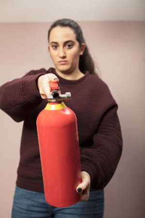 Young woman pointing a red fire extinguisher forwards towards the camera with a serious expression and focus to the canisterの写真素材