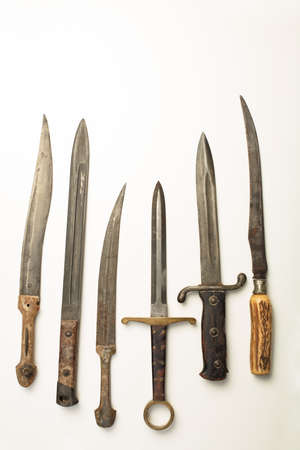 Collection of different vintage knives and daggers with a variety of shapes of blade and hilt or handle laid out in a neat row on white with copy spaceの写真素材