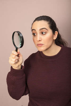 Woman searching for clues or conducting an investigation or search peering through a handheld magnifying glass with a look of concentrationの写真素材