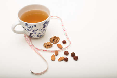 Cup of tea with assorted dried nuts and tape measure viewed from above in a healthy diet and weight loss concept on whiteの写真素材
