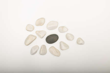 Water washed smooth white pebbles with a single black one on a white background with copy space in a conceptual imageの写真素材
