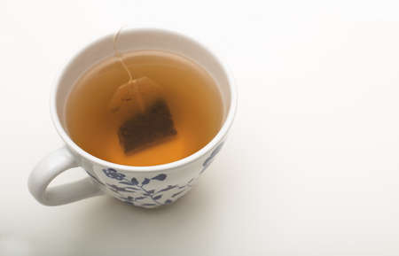Teabag steeping in boiling water in a teacup during the brewing of a relaxing cup of tea over a white backgroundの写真素材