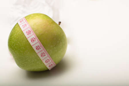 Fresh green apple with a tape measure wound around it in a concept of weight loss through healthy eatingの写真素材