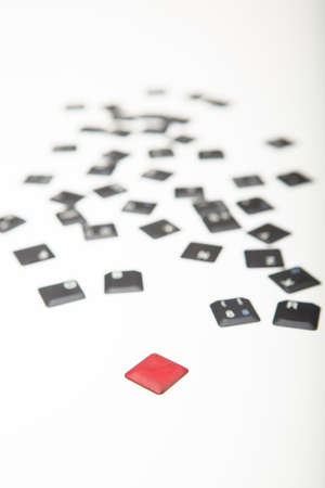 Random scattered loose computer keyboard key covers receding into the distance on a white background with a single red one in the foreground in a conceptual imageの写真素材