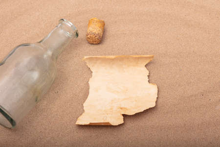 Blank message in a bottle on the beach concept with an opened old glass bottle with loose cork lying beside a blank torn piece of parchment with copy space on the sandの写真素材