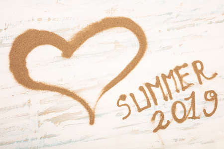 hearth shape of sea sand with 2019 summer text on a vintage blue and white painted wooden backgroundの写真素材
