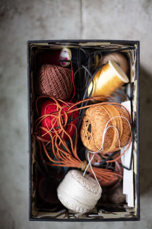 Close up view of assorted twines, string and thread rolls in an open container viewed from overhead on a rustic wood shelf below a window under sunshineの写真素材