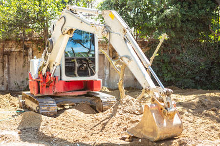 Excavator, backhoe working on soil for clear the area beside trees for new park building