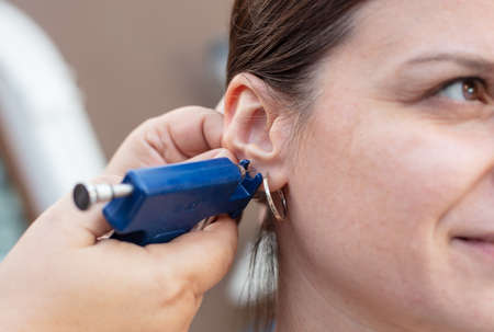 Woman having ear piercing process with special piercing gun in beauty center by medical worker, cropped close up viewの写真素材