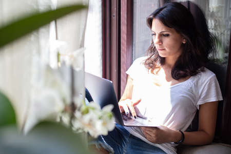 Young woman relaxing on a sunny window with a laptop