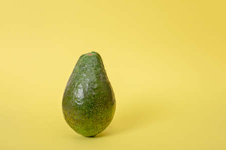 Dark green avocado fruit on yellow background with shadow. Design element for product label.