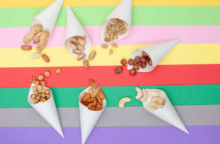 Assorted nuts served in paper cones scattered on a colorful paper background top viewの写真素材