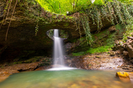Waterfall in the forest with green leaves and a stone in the foreground. Landscape photo of Deliklikaya Waterfall. Located near Murgul, Artvin, Turkeyの写真素材