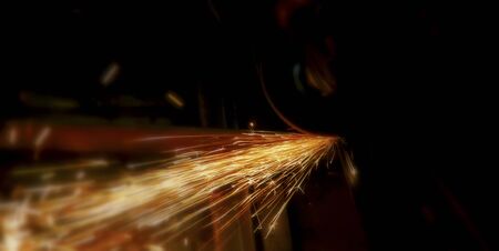 Glowing flow of steel or metal grinding spark particles shine in the dark background.Welder in workshop manufacturing metal construction by cutting to shape using huge orange sparks.Craftsman sawing metal with disk grinder in workshop.Selective focus.の写真素材