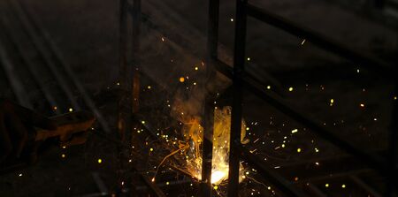 A welder at work in a workshop produces metal structures. Sparks from welding fly around.の写真素材