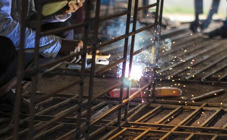 A welder at work in a workshop produces metal structures. Sparks from welding fly around.の写真素材
