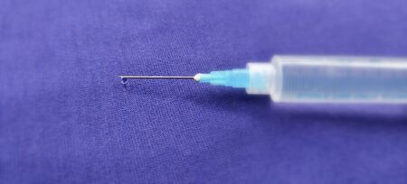 Close-up of a syringe with cannula and drop in front of dark blue backgroundの写真素材