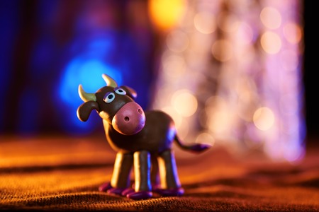 Christmas cow from plasticine on the background of lightsの写真素材