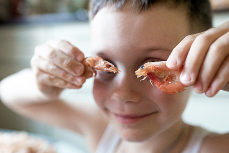 Little boy puts two shrimp to his eyes like glasses and smilesの写真素材