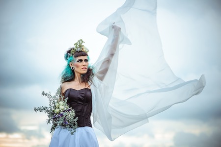 fairy bride with a veil and a wreath holding a bouquet on a blurred backgroundの写真素材