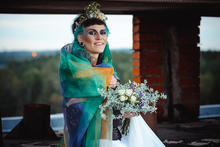 fairy bride with a veil and a wreath holding a bouquet on a blurred backgroundの写真素材