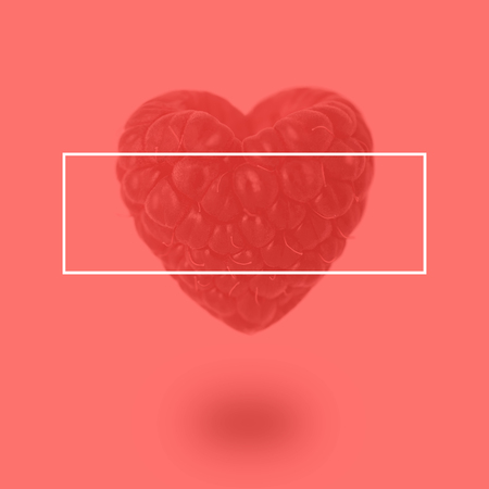 Raspberry in the shape of a heart on a coral backgroundの写真素材