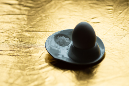 boiled egg with spoon, stand and salt on gold backgroundの写真素材