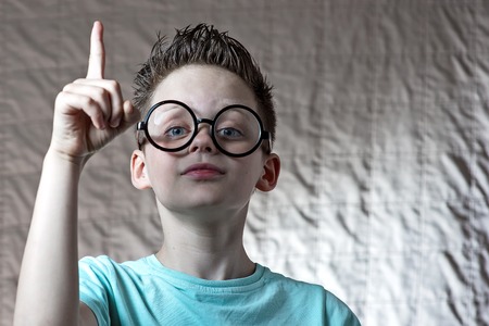 a boy in a light t-shirt and round glasses raised his index fingerの写真素材