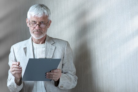 a gray-haired man in light clothes and glasses enters into a contract on paperの写真素材